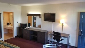 Hotelkamer met een bed, een bureau met stoel, een televisie, een spiegel, een bureaulamp en een deur.