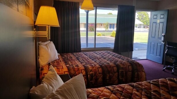Een hotelkamer met een groot bed, twee bedlampjes en uitzicht op de parkeerplaats en het gebouw.
