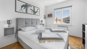 Una camera da letto con un letto, un comodino, una lampada, opere d'arte incorniciate al muro e una finestra con vista sugli edifici.