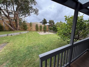 A backyard with a wooden deck, a grassy lawn, and a wooden fence. - Cosy beachside cottage a short walk to the beautiful Coronet Bay beach (Coronet Bay)