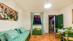 Een gezellige woonkamer met een groene bank, een eettafel met stoelen, een groen kastje en een schilderij aan de muur.