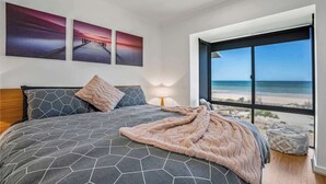 Un dormitori amb un llit gran, vistes a la platja i tres quadres a la paret.