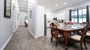 A modern kitchen with white cabinets, a stainless steel refrigerator, and a dining area with a wooden table and chairs. - Spacious 6bdr/5bath Vacation Home 1 mi to beach (Naples)
