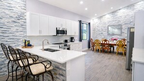 A modern kitchen with white cabinets, a central island with bar stools, a dining area with wooden chairs, and a stone backsplash. - Spacious 6bdr/5bath Vacation Home 1 mi to beach (Naples)