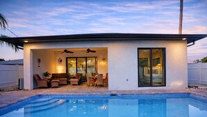A modern house with a swimming pool, patio furniture, and a covered outdoor seating area. - Spacious 6bdr/5bath Vacation Home 1 mi to beach (Naples)