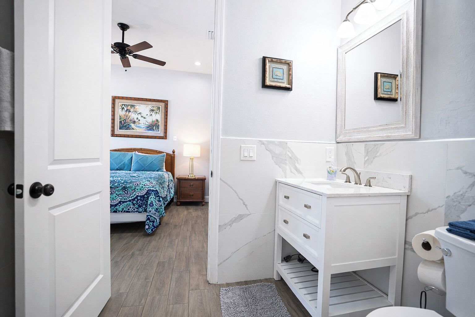 A hotel room with a bed, bedside table, nightstand, and a bathroom with a sink and mirror.