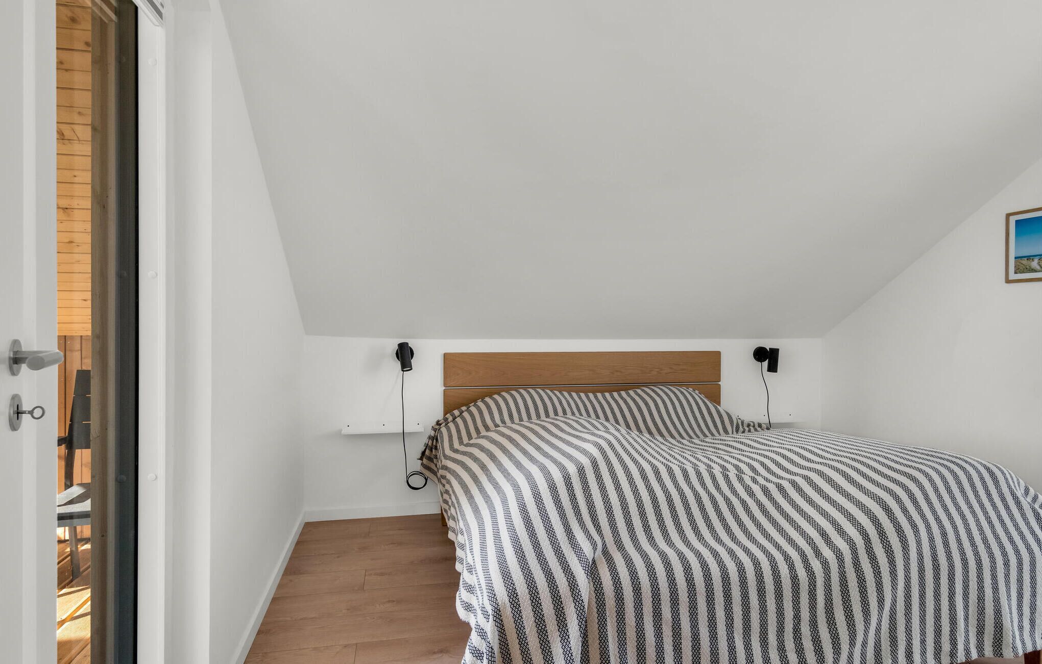 A bedroom with a wooden headboard, a bed with a patterned bedspread, a bedside table, and a wall-mounted lamp.