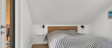 A bedroom with a wooden headboard, a bed with a patterned bedspread, a bedside table, and a wall-mounted lamp.