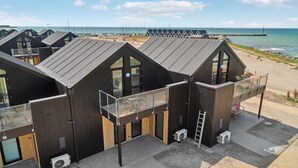 En række moderne strandhuse i mørkt træ med store vinduer og balkoner, beliggende på en sandstrand med havet i baggrunden.