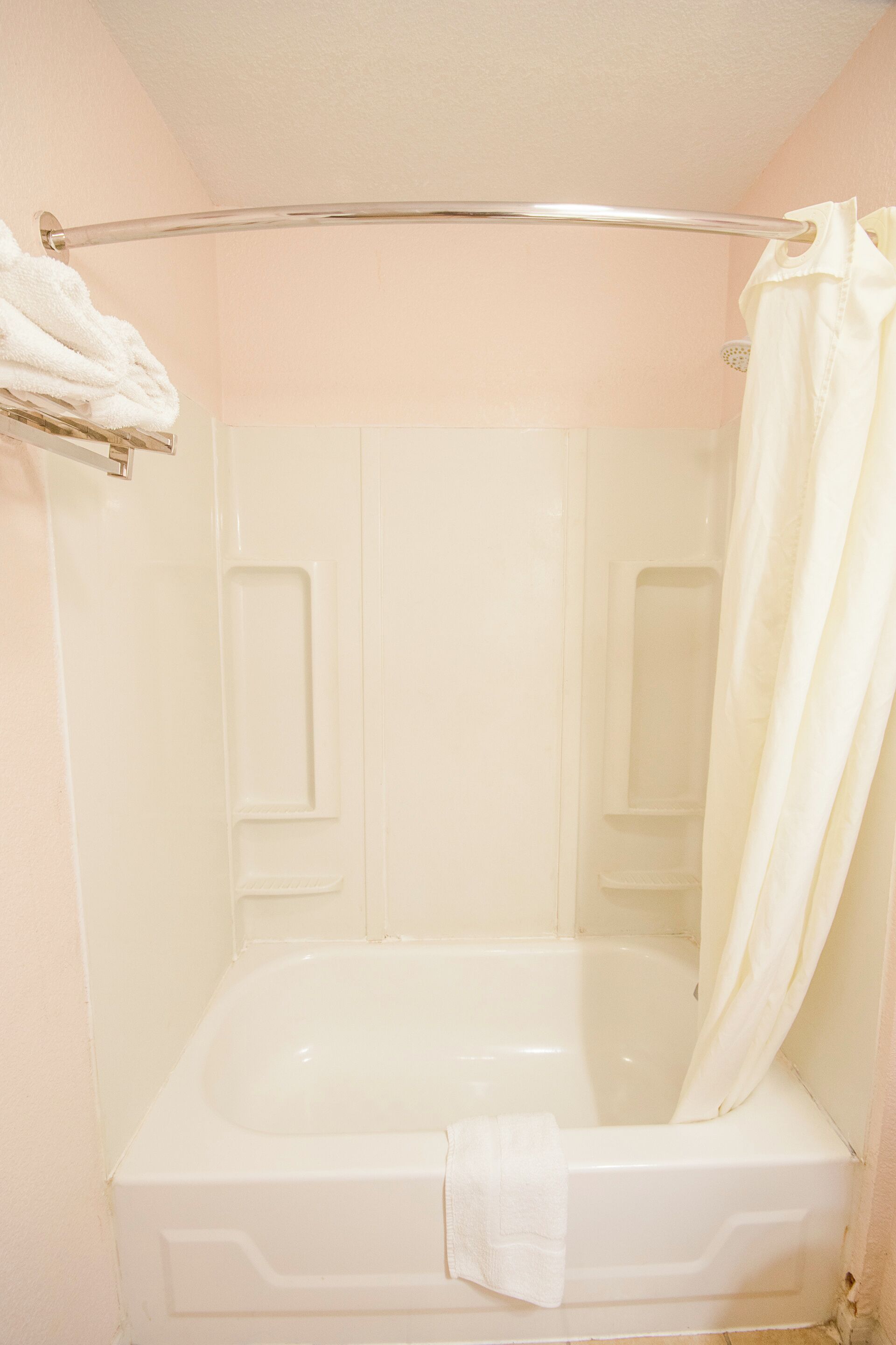 Una bañera blanca con cortina de ducha, toallero y cabezal de ducha.