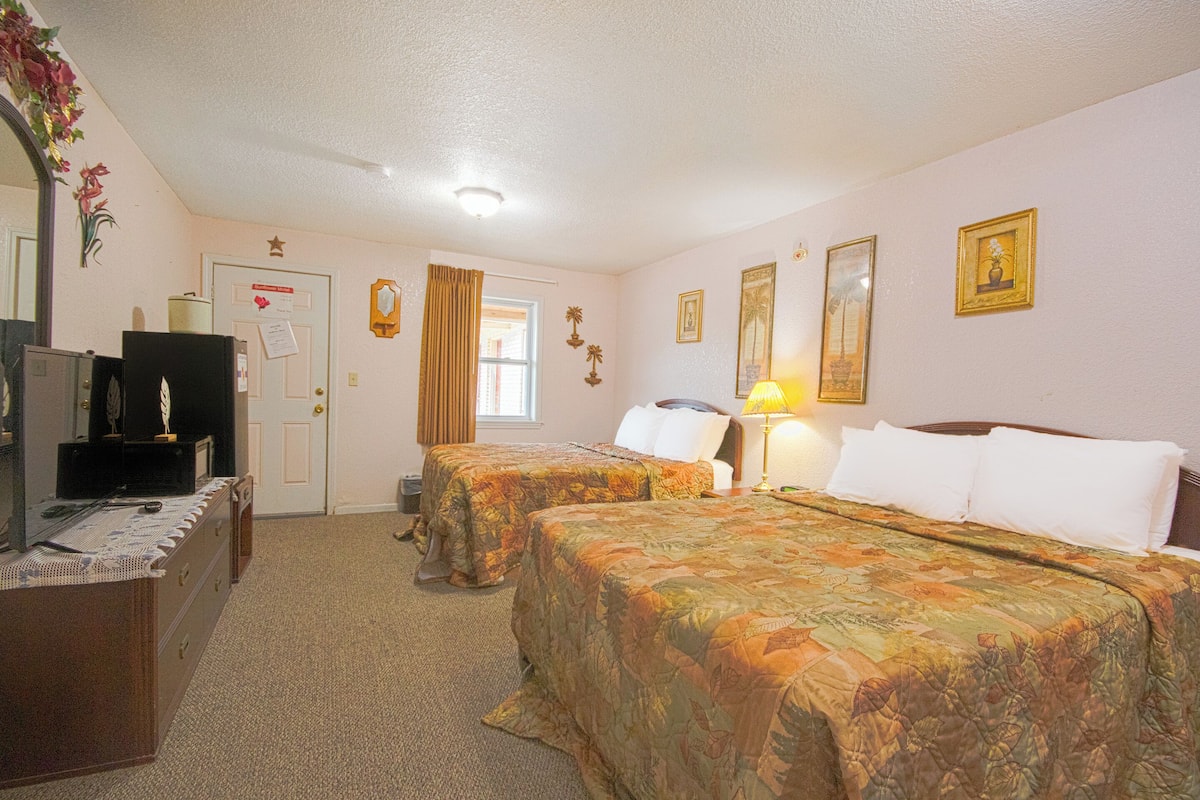 A hotel room with two beds, a desk, a dresser, a mirror, and a door with a star decoration.