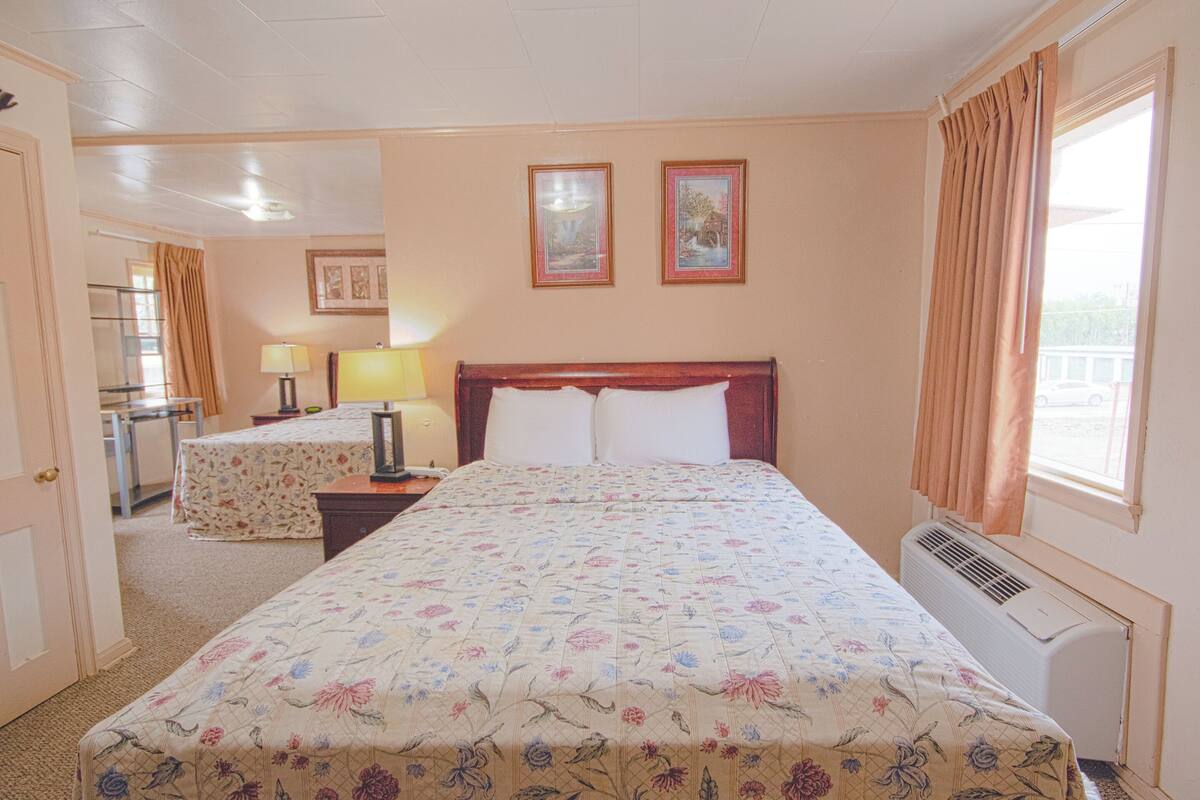 A hotel room with a large bed, a desk, a chair, a lamp, and two framed pictures on the wall.