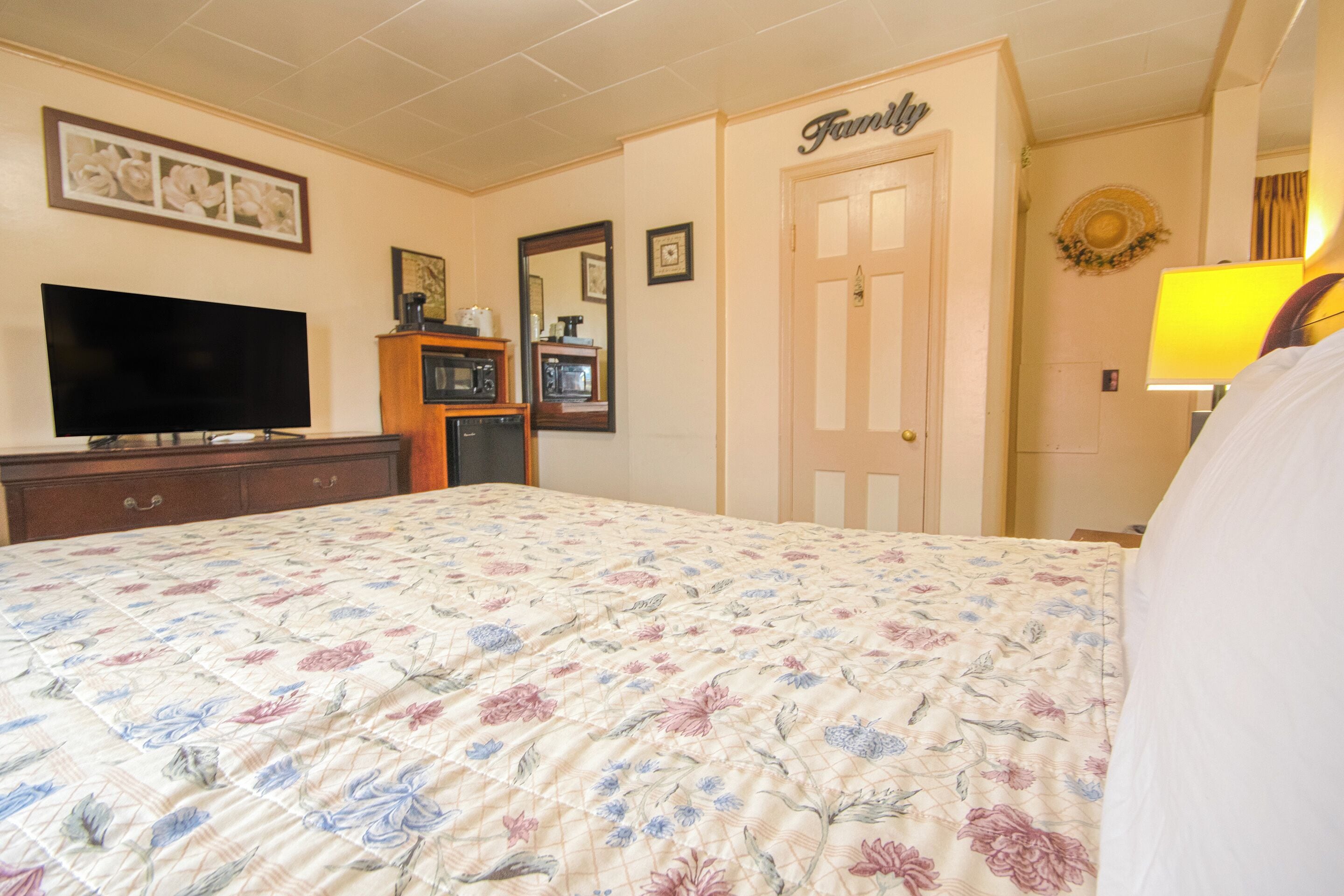 Un dormitorio con colcha estampada, televisor de pantalla plana, cómoda, espejo y una puerta con la leyenda 'Familia'.