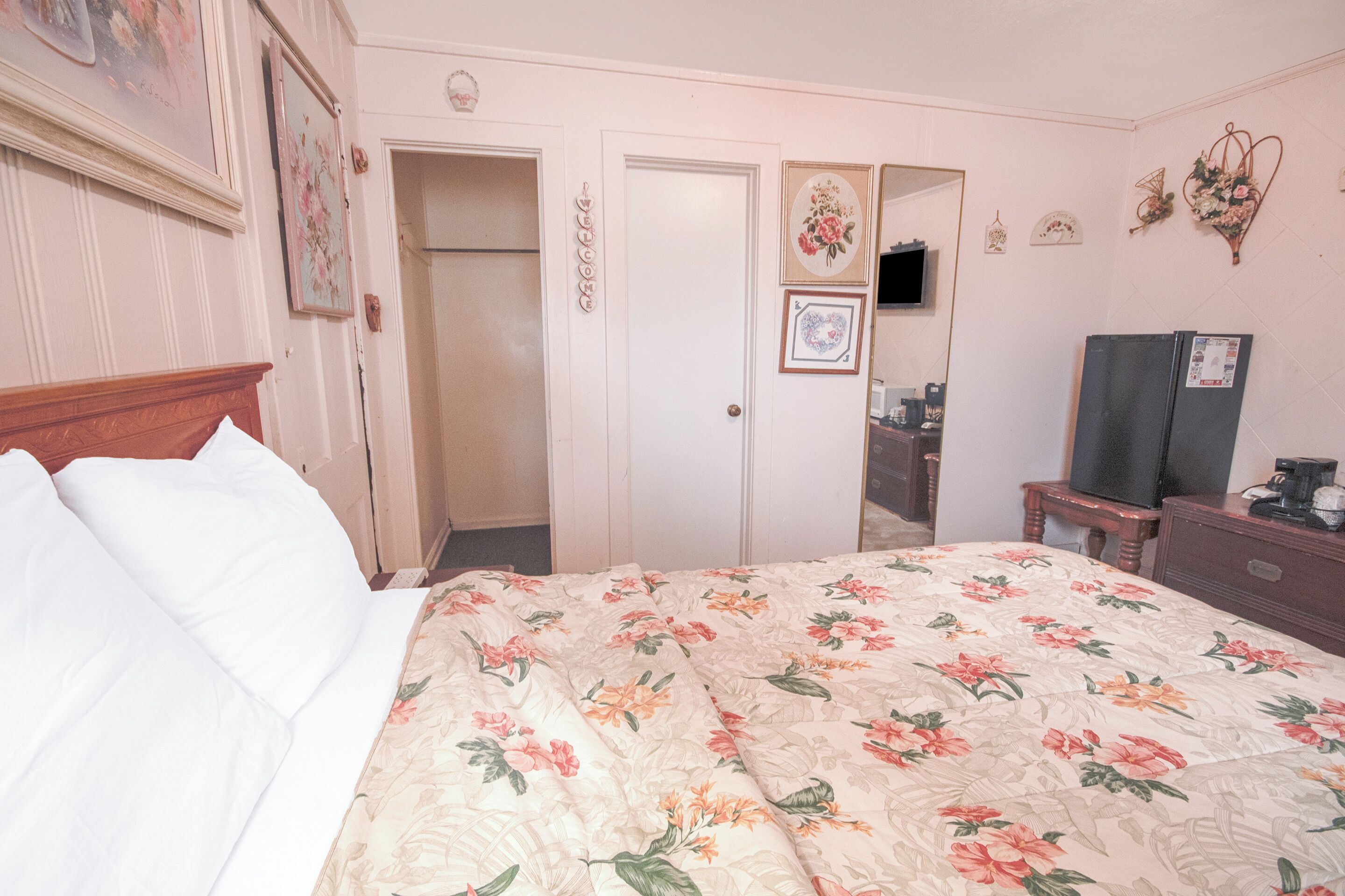 Un dormitorio con colcha estampada, cabecero de madera, armario, espejo y cómoda con televisor.
