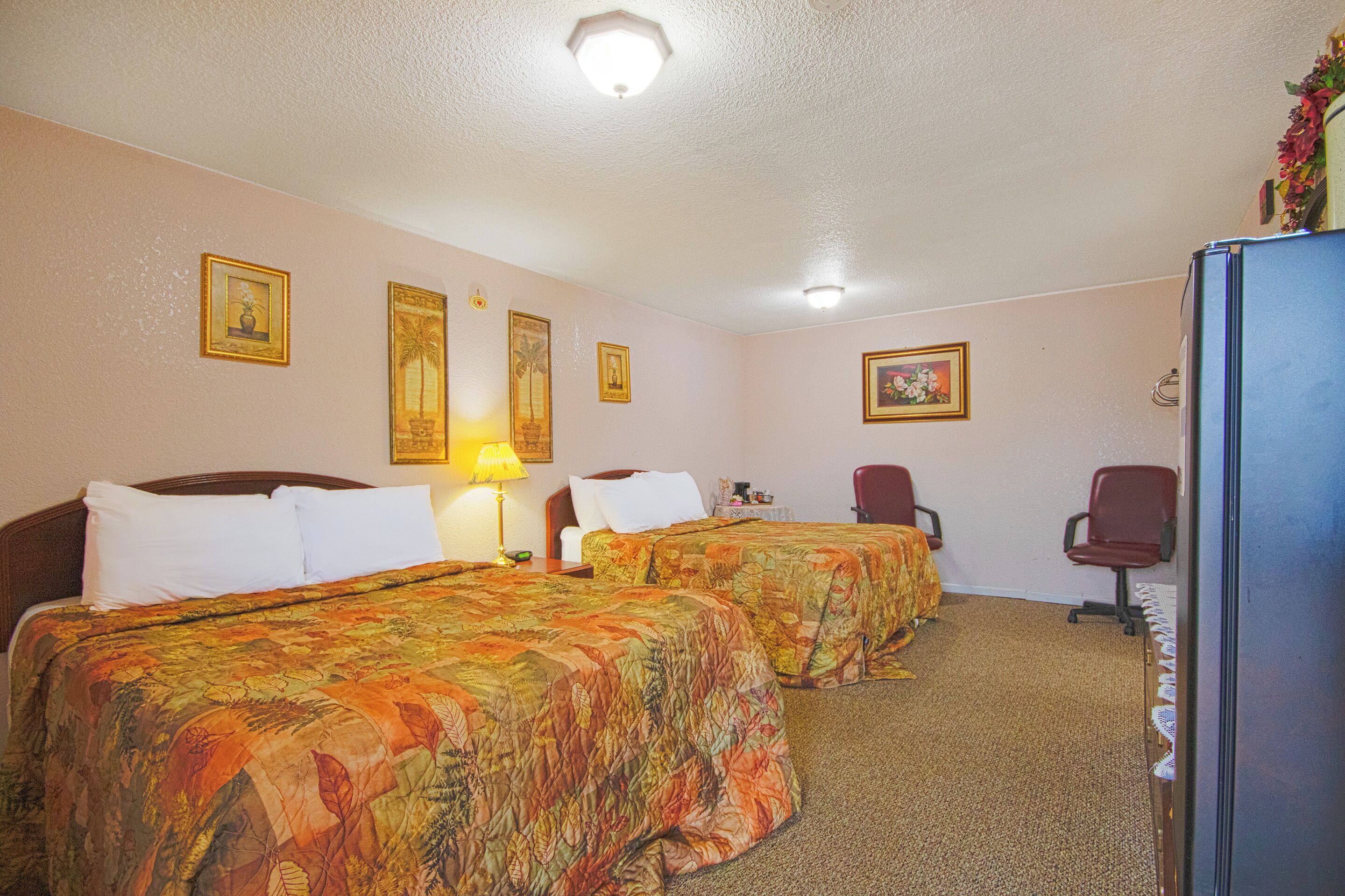 Quarto de hotel com duas camas, um frigorífico, uma escrivaninha e uma cadeira.