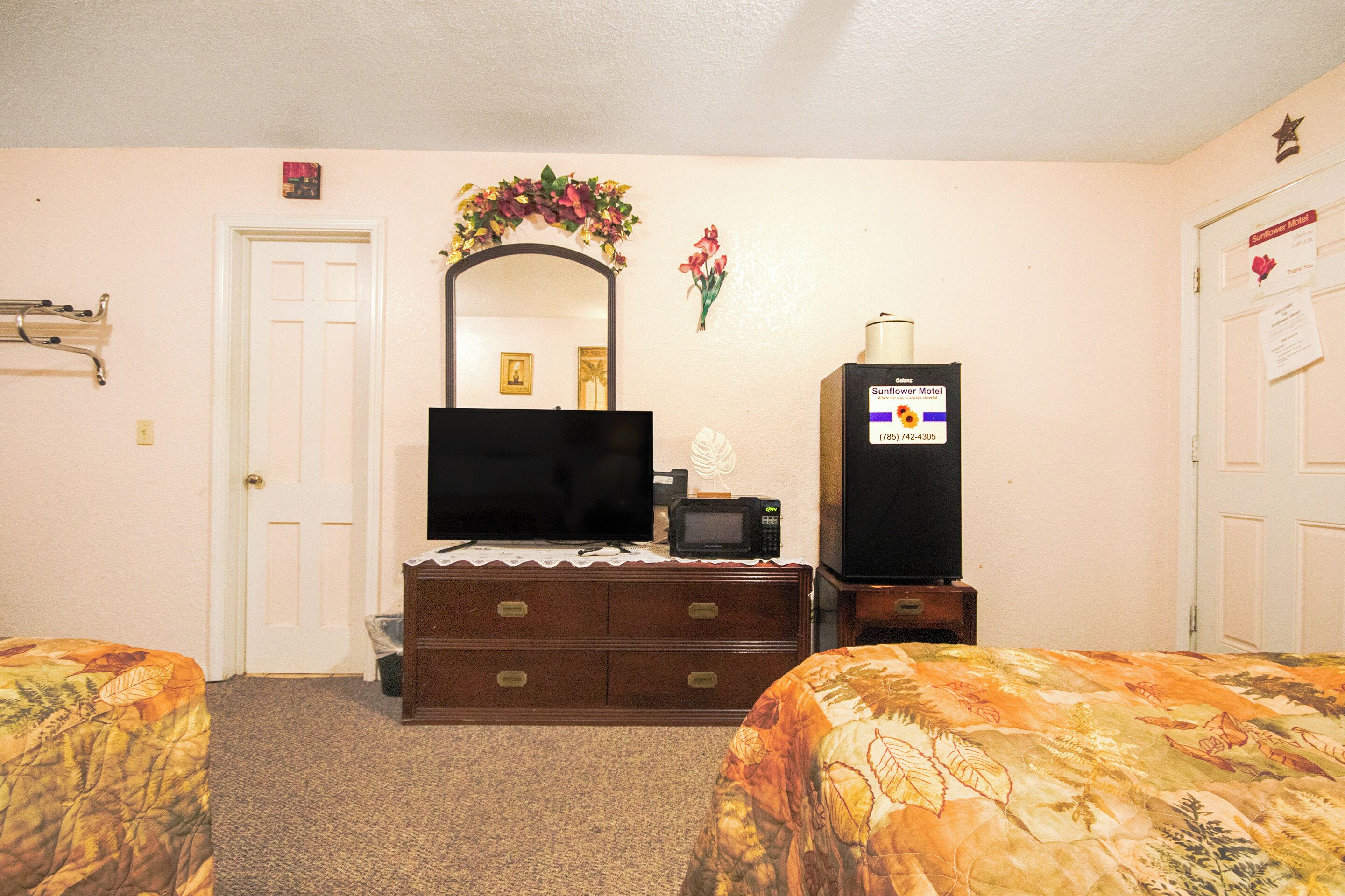 A hotel room with a bed, a dresser, a television, a microwave, and a refrigerator.