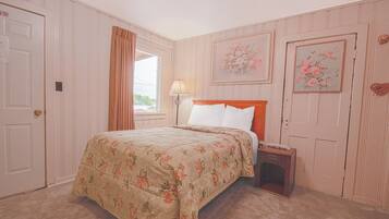 Une chambre à coucher avec une couvre-lit à motifs floraux, une table de chevet avec une lampe et deux tableaux floraux encadrés accrochés aux murs.