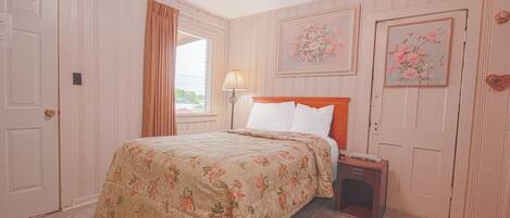 Une chambre à coucher avec une couvre-lit à motifs floraux, une table de chevet avec une lampe et deux tableaux floraux encadrés accrochés aux murs.