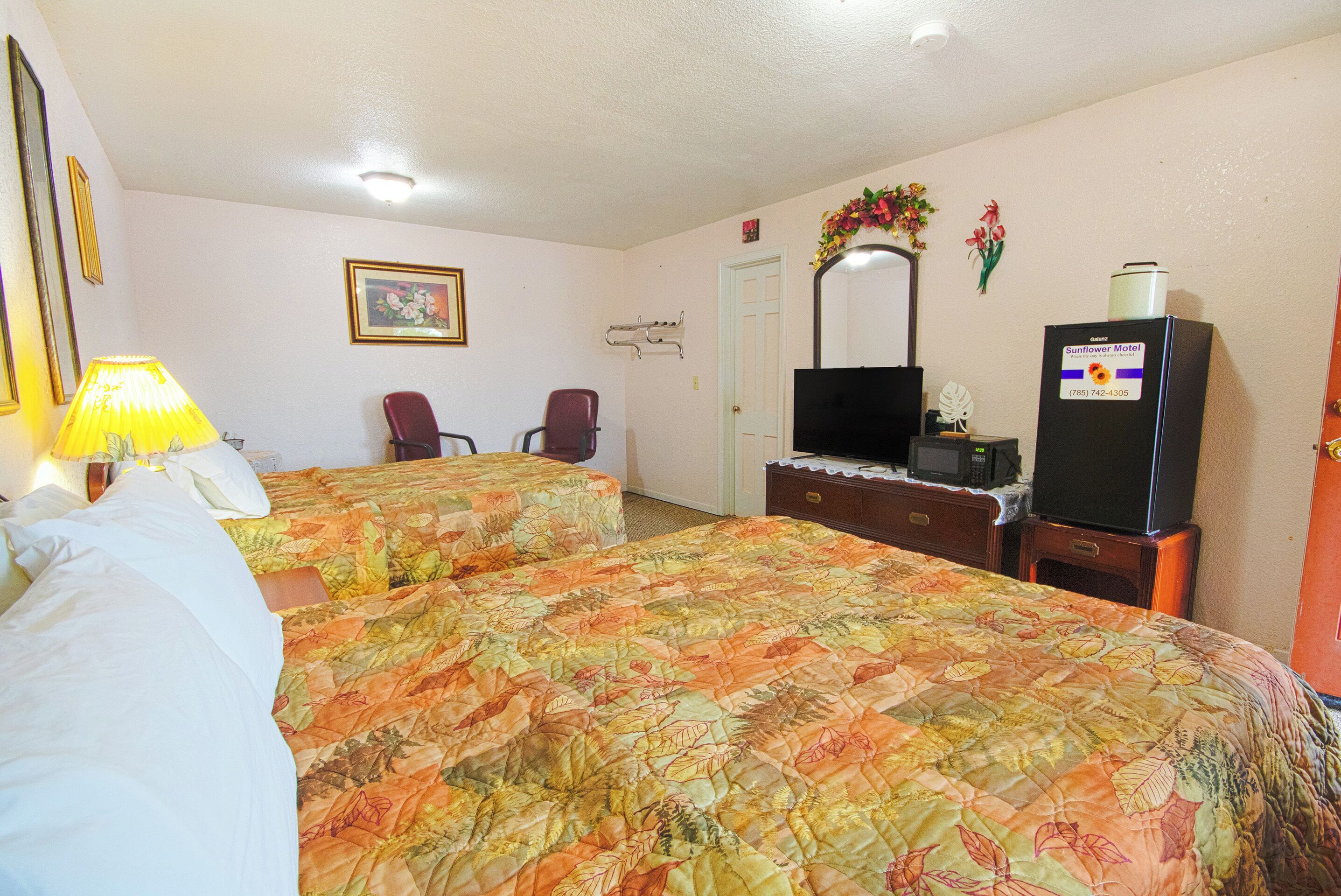 A hotel room with two beds, a desk, a chair, a TV, and a refrigerator.
