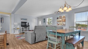 A modern living room with a grey sofa, teal dining table, and wooden flooring. - Guest Favorite- walk to the beach! (Salvo)