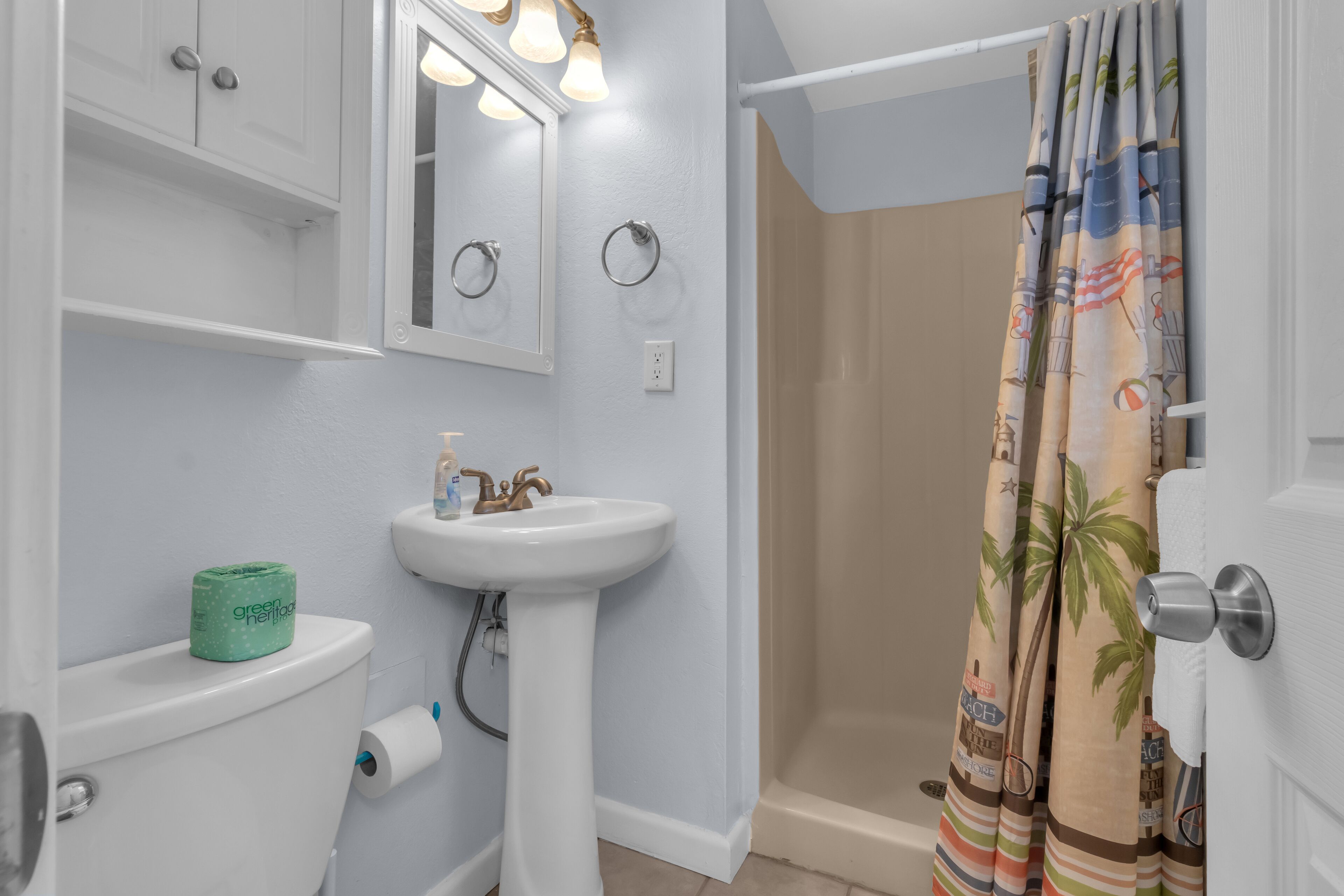 Une salle de bain équipée de toilettes, d’un lavabo, d’un miroir et d’un rideau de douche.
