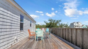 A wooden deck with a table and chairs, a wooden fence, and a house in the background. - Guest Favorite- walk to the beach! (Salvo)