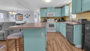 A modern kitchen with teal cabinets, a central island, a built-in oven, and a dishwasher. - Guest Favorite- walk to the beach! (Salvo)