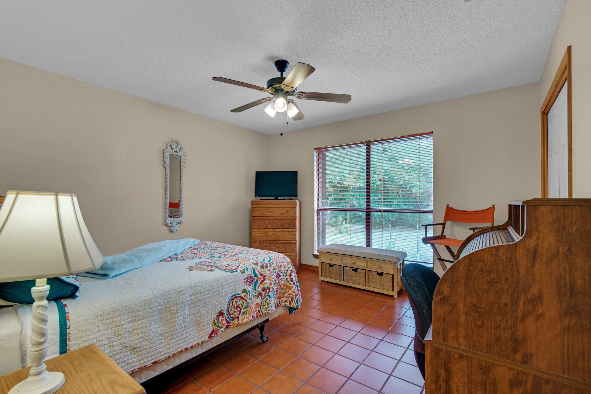 A bedroom with a bed, dresser, chair, and a ceiling fan.