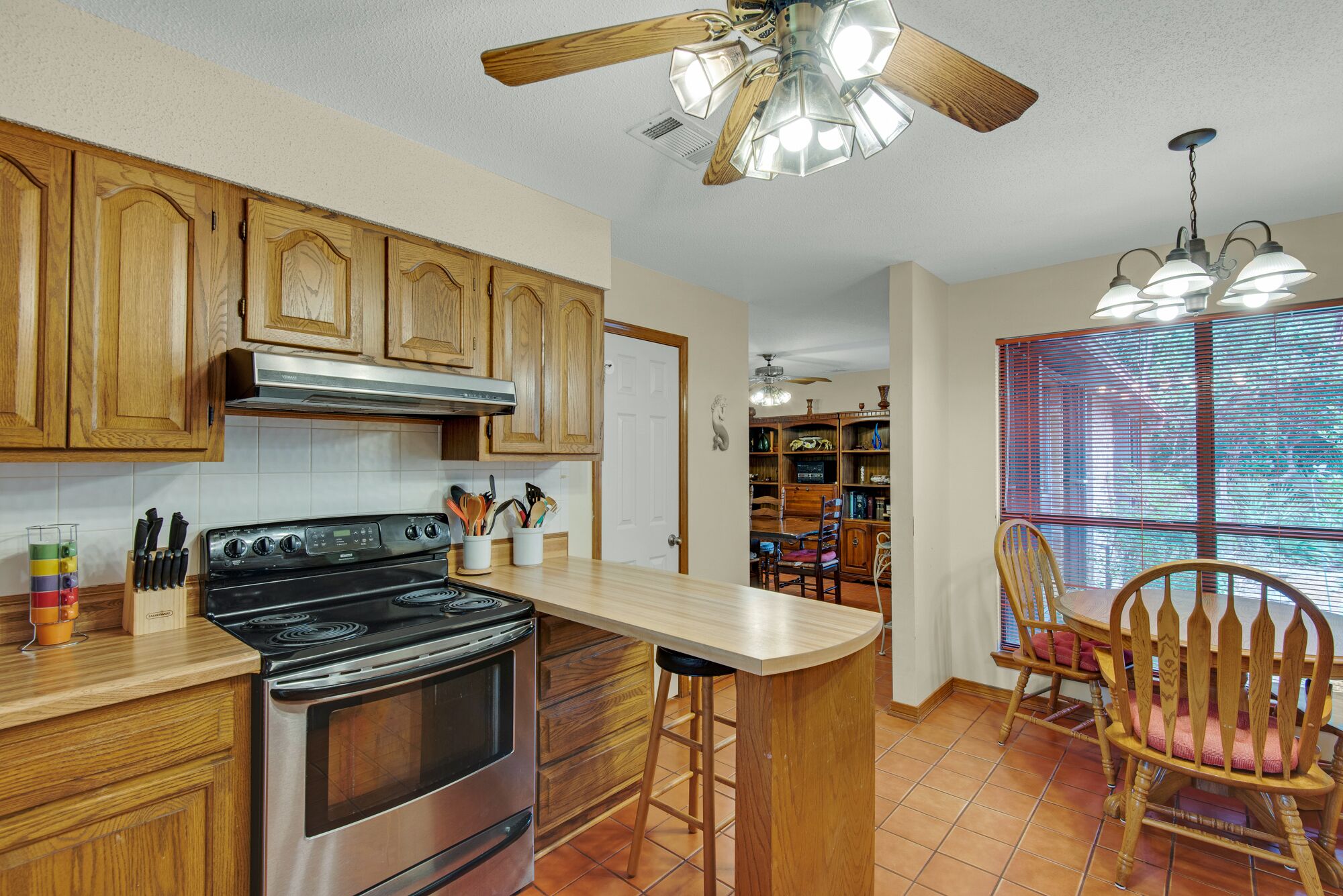 A kitchen with wooden cabinets, a stainless steel stove, and a bar area with a chair.