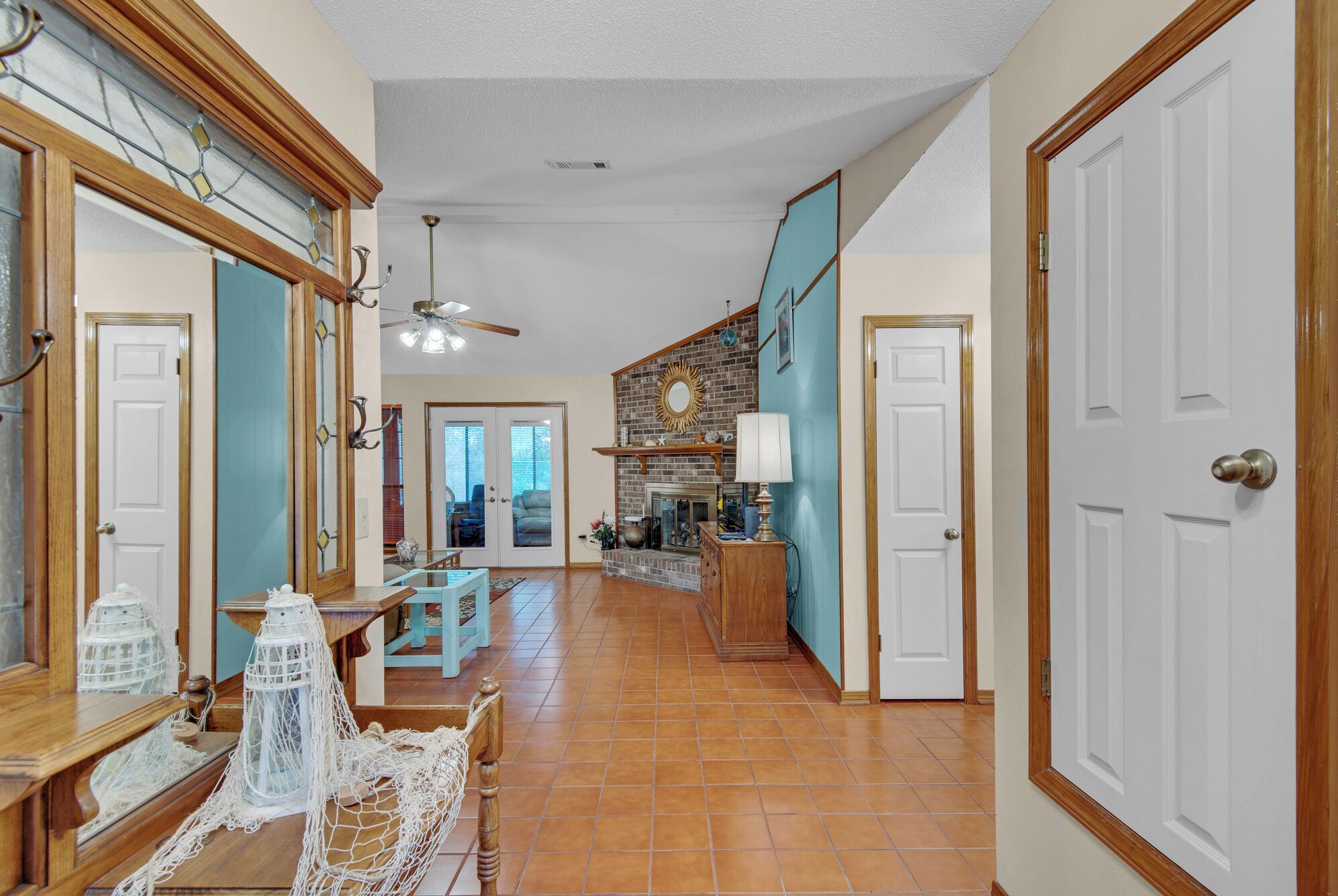 A spacious hallway with a tiled floor, wooden doors, and a brick fireplace.