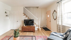 A living room with a wooden coffee table, a sofa, a TV, and a staircase. - Sunny & Stylish Manayunk Cottage w/ Private Back Yard (Philadelphia)