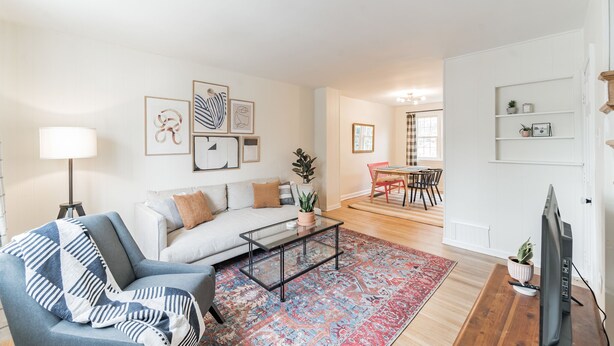 A living room with a sofa, coffee table, and a TV on a wooden stand. There is a dining area with a table and chairs. - Sunny & Stylish Manayunk Cottage w/ Private Back Yard (Philadelphia)