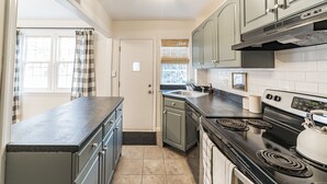 A kitchen with a black stove, a sink, and light green cabinets. - Sunny & Stylish Manayunk Cottage w/ Private Back Yard (Philadelphia)