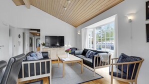 Una sala de estar moderna con techo de madera, un televisor grande, un sofá, una mesa de centro y vistas al exterior.