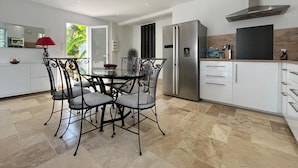 Een moderne keuken met witte kasten, een roestvrijstalen koelkast en een eethoek met een glazen tafel en metalen stoelen.