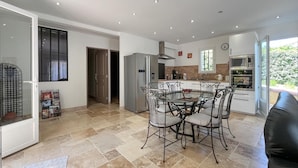Een moderne keuken met een centraal eiland, roestvrijstalen apparatuur en een eethoek met metalen stoelen.