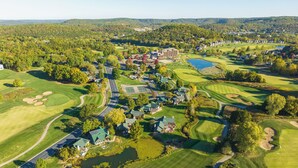 Vista aérea de un campo de golf con un club de campo, varias edificaciones y zonas boscosas circundantes.