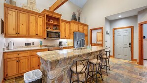 Cocina con gabinetes de madera, encimera de granito, refrigerador de acero inoxidable e isla de piedra con taburetes de bar.