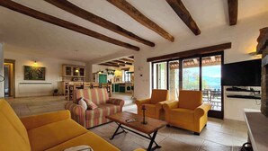A spacious living area with yellow sofas, a striped sofa, and a wooden coffee table. There is a kitchen in the background with a view of the outdoors. - Villa with pool and air conditioning (Bartolići)