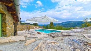A stone pool with lounge chairs and umbrellas, surrounded by a stone wall and a view of mountains. - Villa with pool and air conditioning (Bartolići)