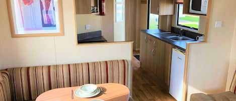 Una kitchenette compacta con microondas, pileta y alacenas. En primer plano, una mesa de comedor con platos y cubiertos.