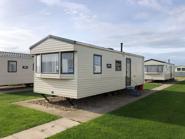 A mobile home with a front porch, a small attached garage, and a window with a curtain. - Golden Anchor Holiday Park (Skegness)