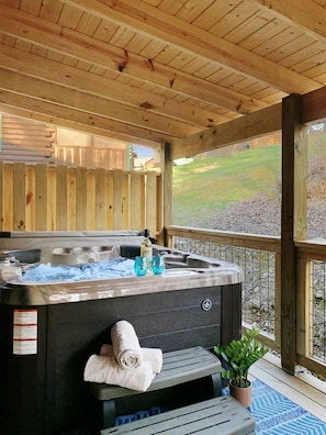 A hot tub with a wooden deck, a towel, and a bottle of shampoo. - Cozy 3BDR Cabin Across From Convention Center | Fast WiFi | Hot Tub (Sevierville)
