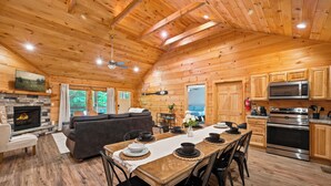 Interior de una cabaña de troncos con comedor, cocina, sala de estar, chimenea y ventanas amplias.