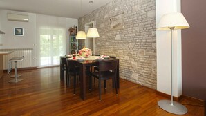 A dining area with a stone wall, a wooden floor, and a modern chandelier. - Villa with air conditioning and pool (Pula)