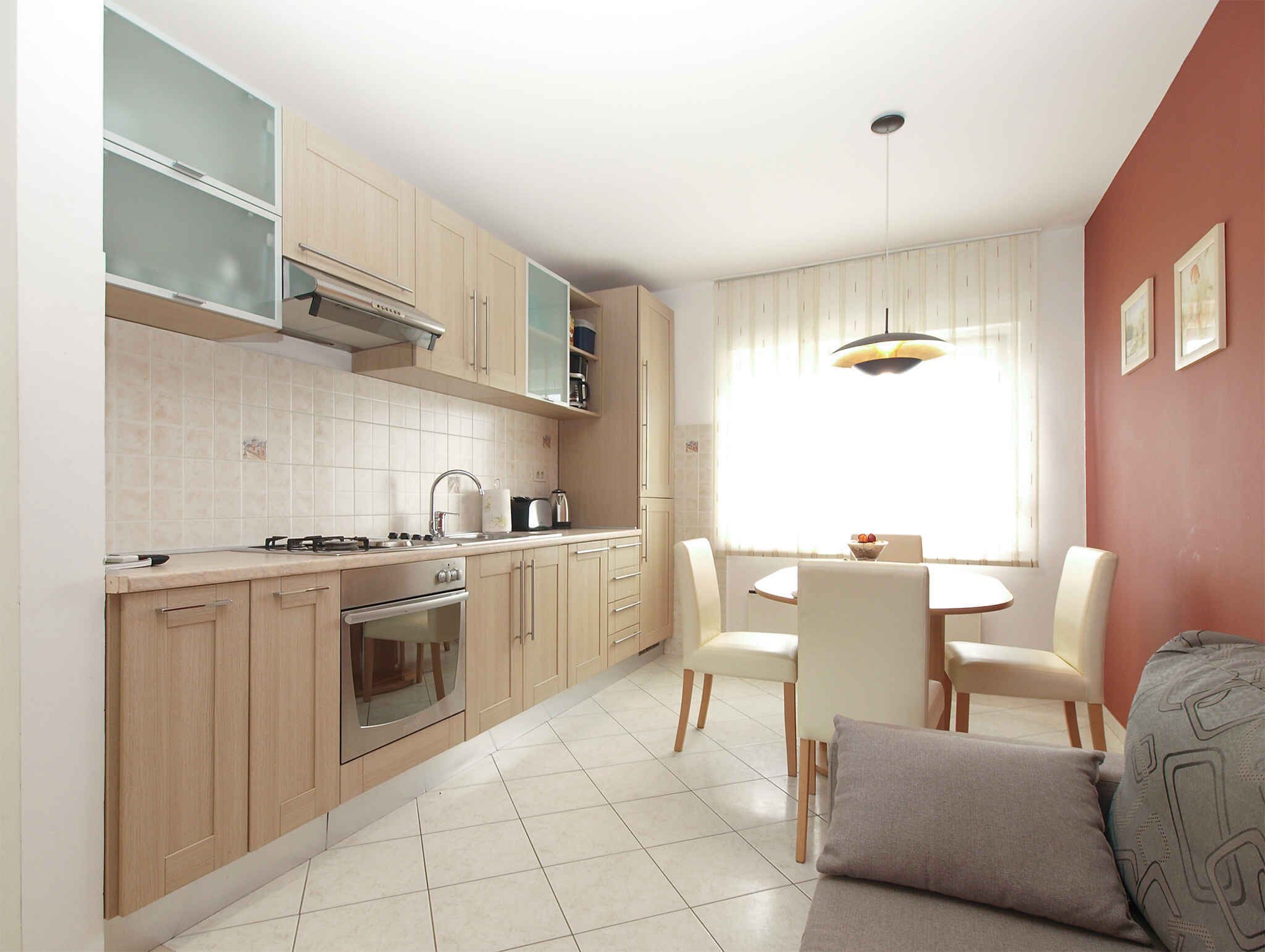 Una cocina moderna con armarios de madera clara, una estufa a gas, un horno y un comedor con mesa y sillas.