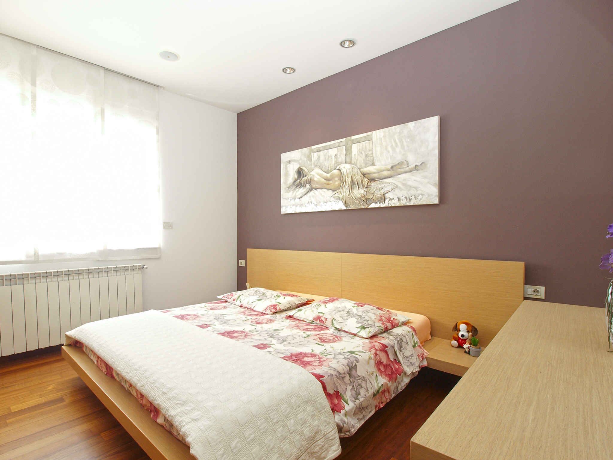 Une chambre à coucher avec un lit, une table de chevet, un tableau accroché au mur et une fenêtre avec des rideaux.