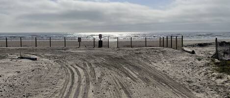 A sandy beach with tire tracks leading to a fence.