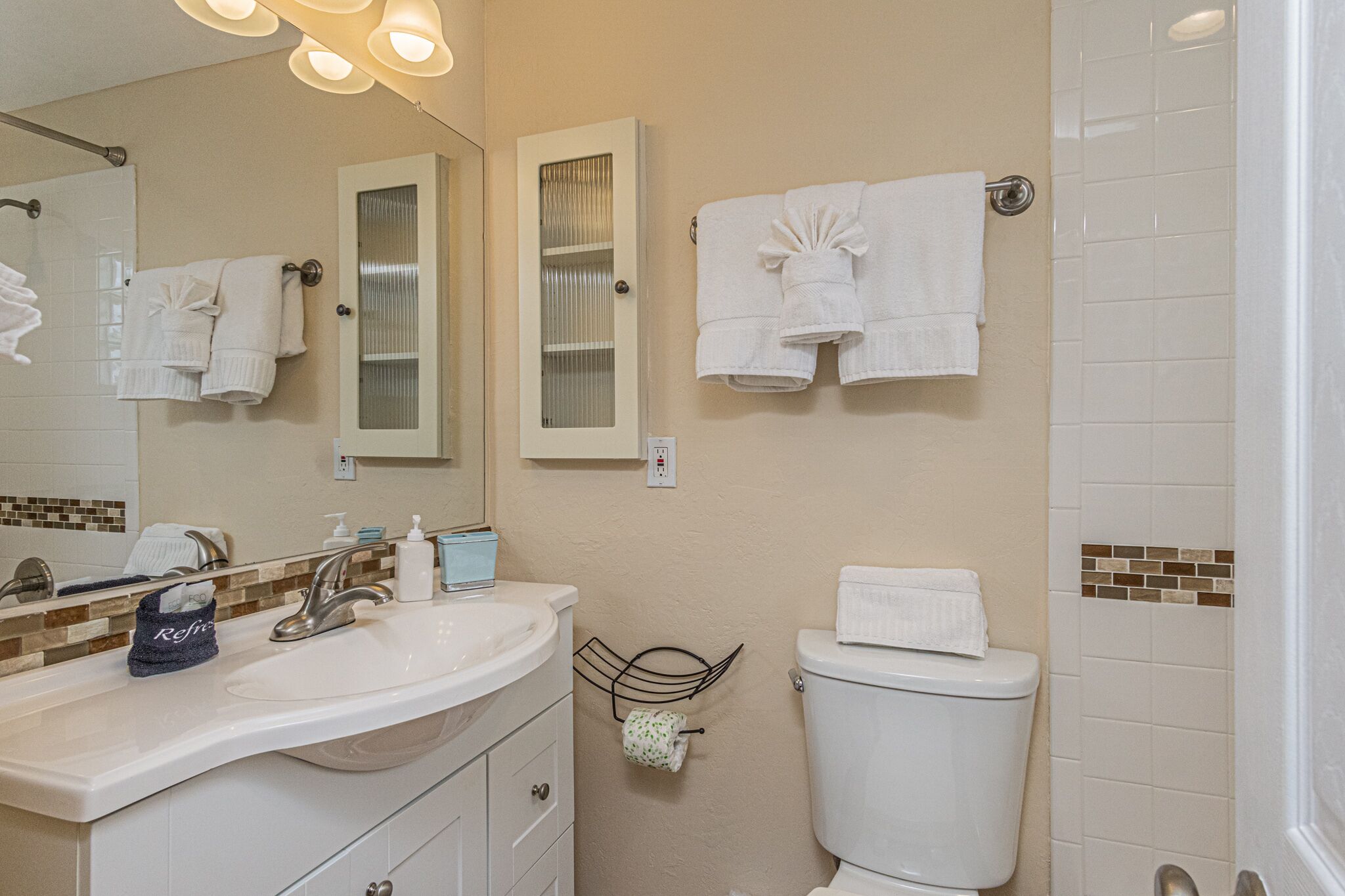 Een badkamer met een wit wastafel, spiegel en toilet, met handdoeken aan de muur.