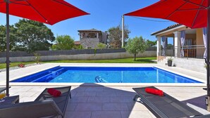 A swimming pool with red umbrellas, lounge chairs, and a stone building in the background. - Villa with swimming pool and table tennis (Divšići)